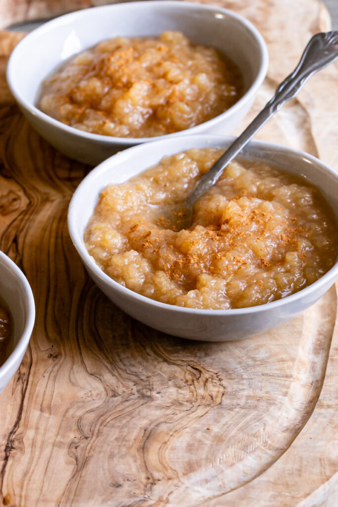 3/4 view of a bowl of golden delicious applesauce with a spoon in it and a bowl behind it