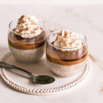 3/4 view of two glasses of caramel eggnog chia pudding topped with vegan caramel, maple syrup and whipped cream