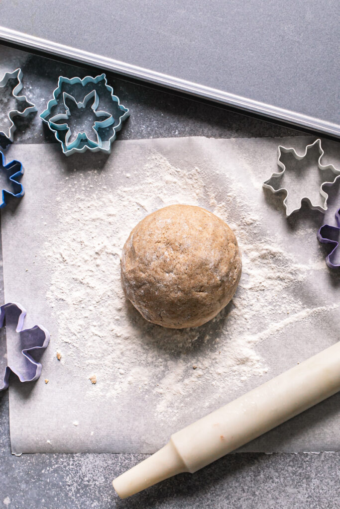 a ball of sugar cookie dough on a piece of parchment paper with a rolling pin, snowflake cookie cutters, and a baking sheet
