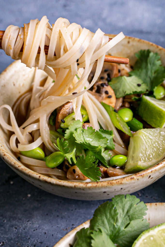 a close up 3/4 shot of pulling rice noodles out of the mushroom pho with chopsticks