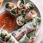 sesame kale spring rolls in a bowl, some cut in half to reveal the filling, served with a bowl of sweet and sour sauce