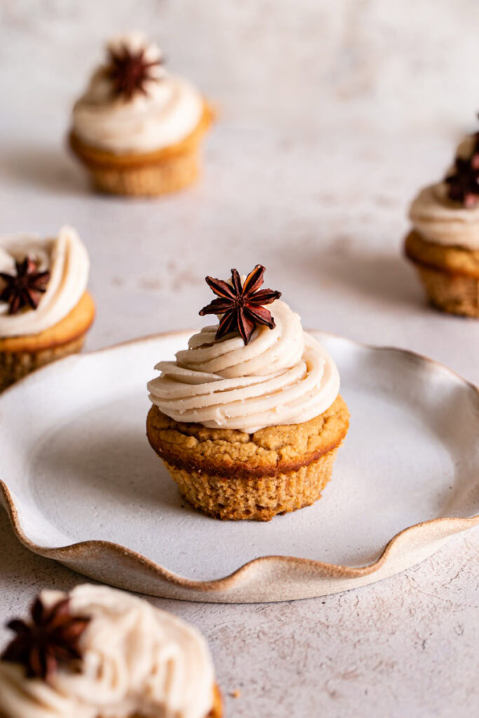 3/4 shot of frosted chai cupcakes with star anise on top, one cupcake in the middle on a plate