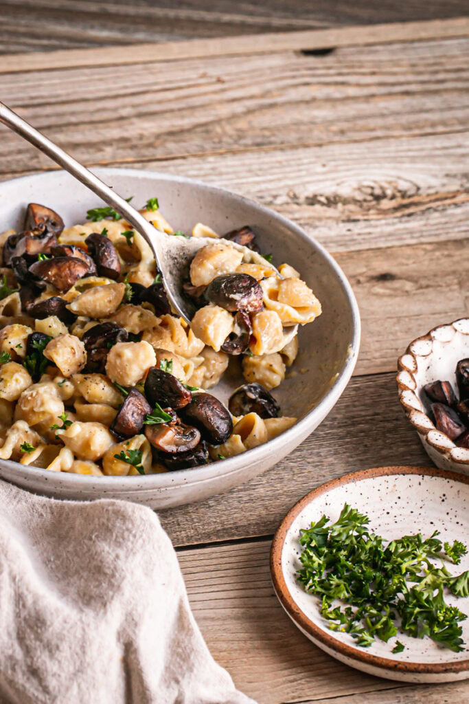 3/4 view of a bowl of Creamy Alfredo Style Mushroom Pasta with a plate of fresh chopped parsley next to it