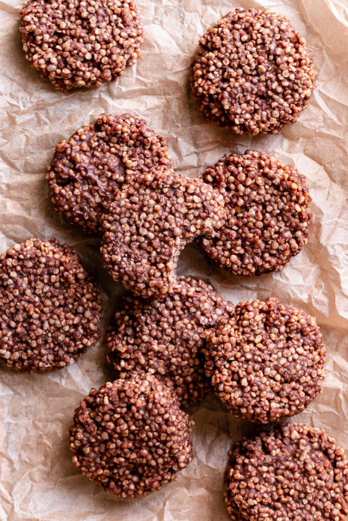 Crispy Quinoa Cacao Cookies  piled on a piece of parchment paper, one with a bite taken out of it