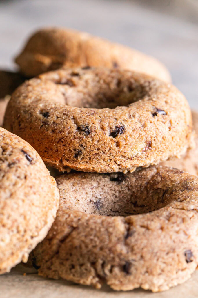 close up vertical image of grain-free banana bread donuts piled on a round wire cooling rack.