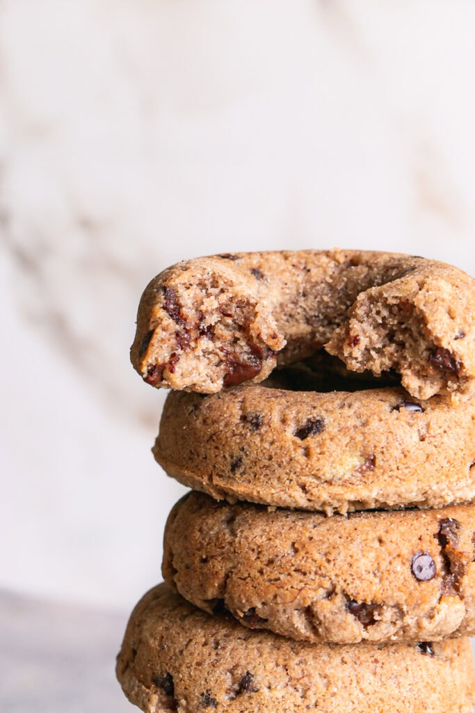 close up of grain-free banana bread donuts stacked on top of one another, the top one with a bite taken out of it.