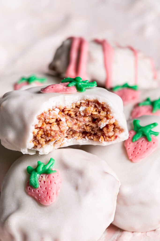 close up 3/4 photo of strawberries and cream qunioa cookies stacked on top of one another, the top one with a bite taken out if it to reveal the crispy inside