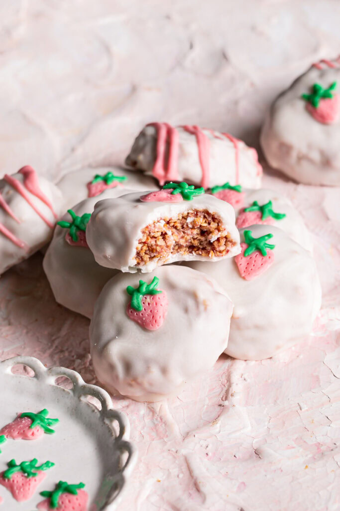 3/4 photo of strawberries and cream qunioa cookies stacked on top of one another, the top one with a bite taken out if it to reveal the crispy inside