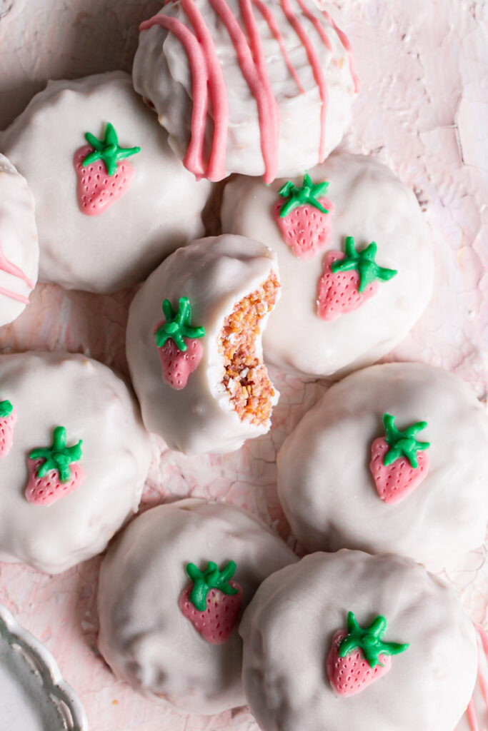 white chocolate covered strawberries and cream qunioa cookies decorated with a painted white chocolate strawberry , the middle cookie has a bite taken out of it to reveal the crispy inside