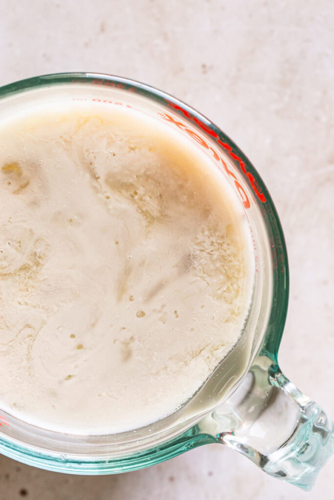 close up shot of a glass measuring cup filled with flax milk mixed with apple cider vinegar