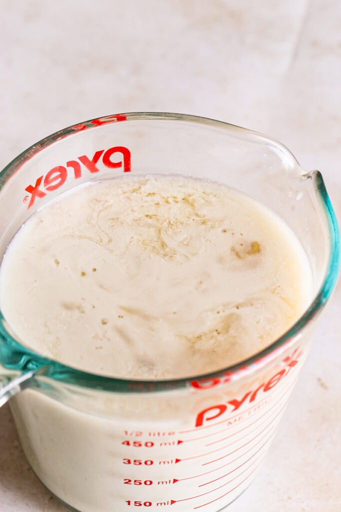 3/4 photo of a glass measuring cup filled with flax milk mixed with apple cider vinegar
