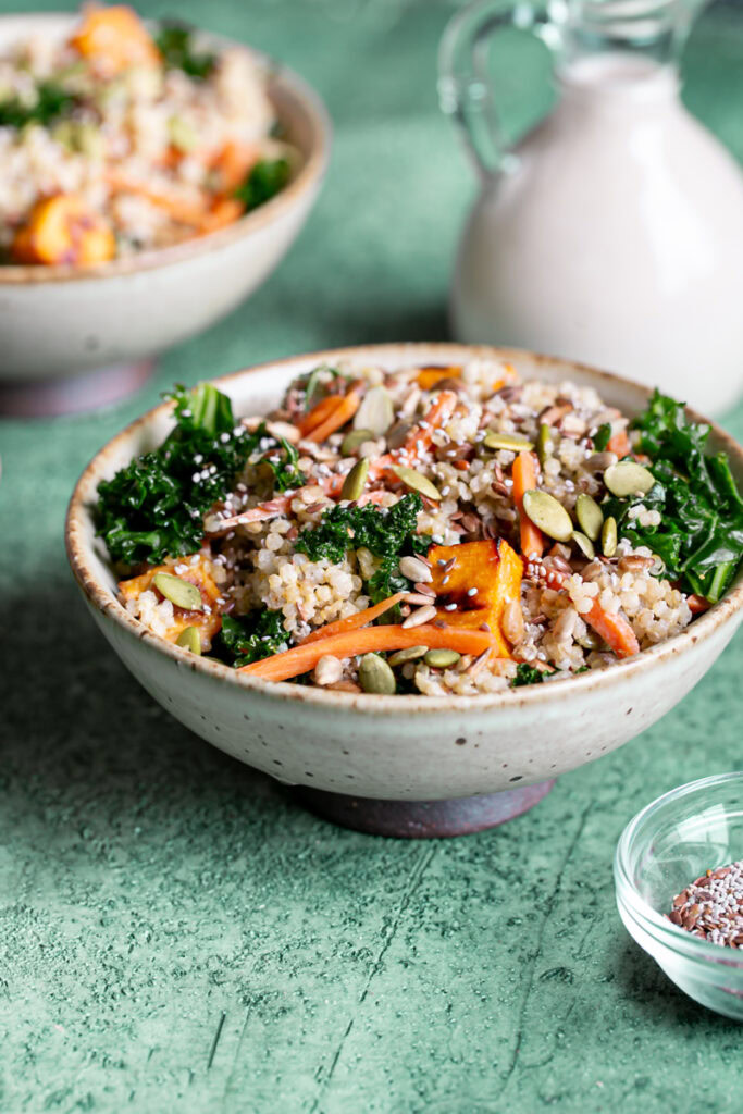 3/4 shot of a bowl of protein-packed creamy tahini bowl with another bowl blurred in the background and a bottle of dressing behind it