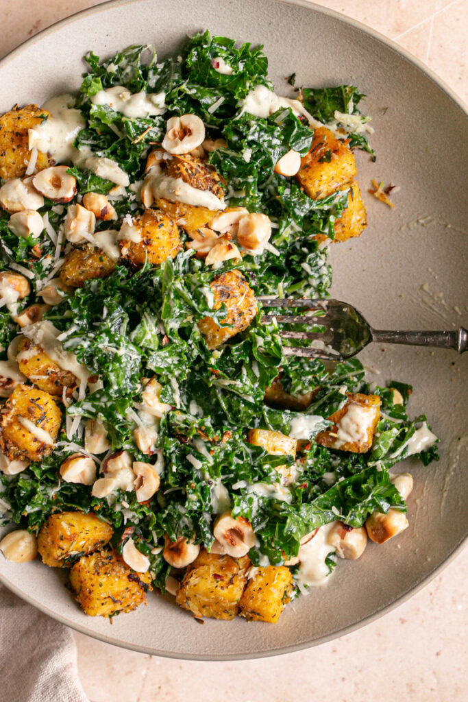 extreme close up of the Kale Caesar Salad with Polenta Croutons and Toasted Hazelnuts with a fork in it and some of the salad already eaten