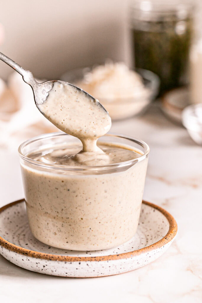 a small glass with caesar dressing and some dripping off a spoon back into the glass
