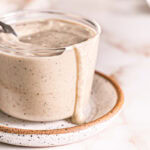 close up shot of a glass full of caesar dressing with a spoon in it and some dripping down the side