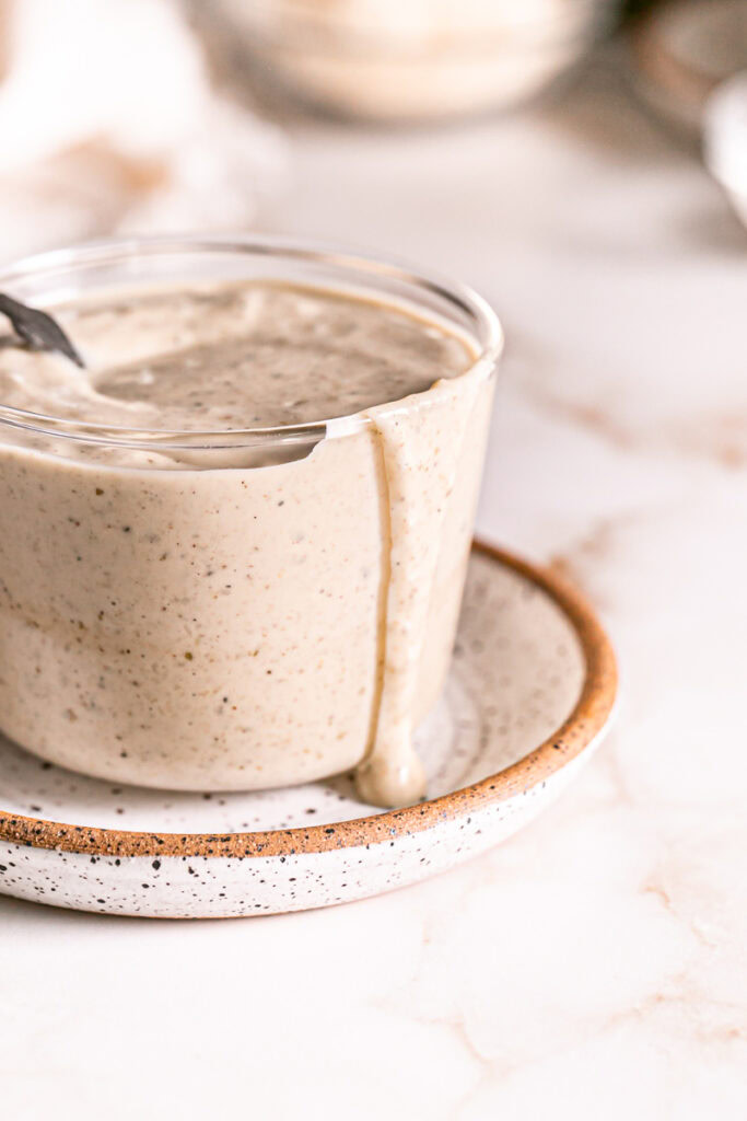 close up shot of a glass full of caesar dressing with a spoon in it and some dripping down the side