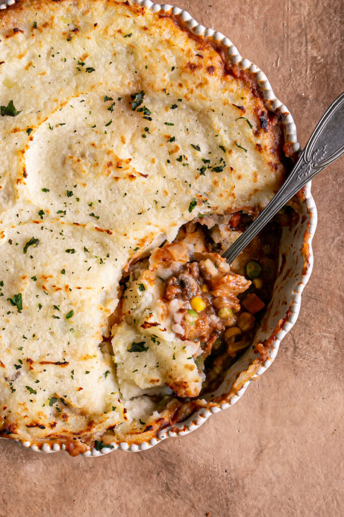 Easy Vegan Gluten-Free Shepherd's Pie with some spooned out of it to reveal the vegetable filling and a spoon sticking out of the dish