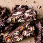 a close up of a Pretzel Pumpkin Seed Date Chocolate Cluster cut in half to reveal the pretzels, pumpkin seeds and dates inside the chocolate