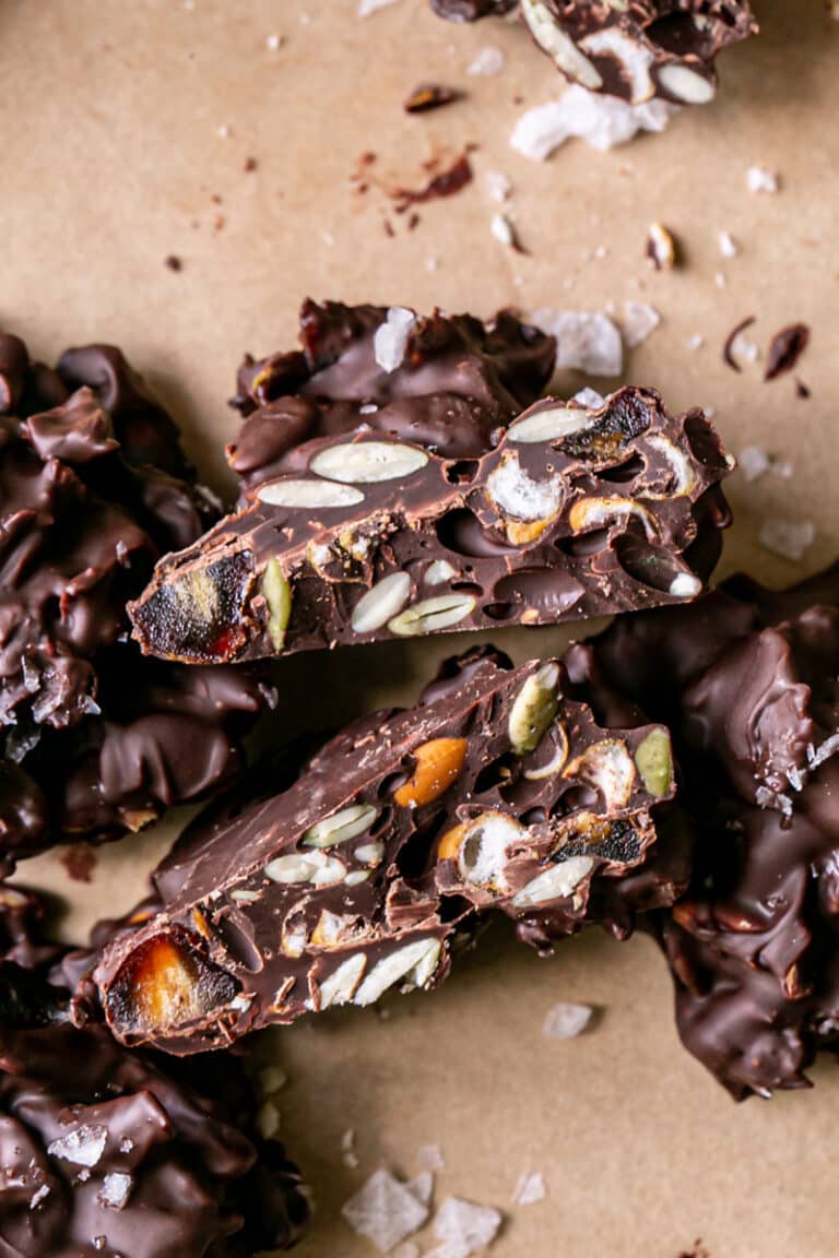 a close up of a Pretzel Pumpkin Seed Date Chocolate Cluster cut in half to reveal the pretzels, pumpkin seeds and dates inside the chocolate