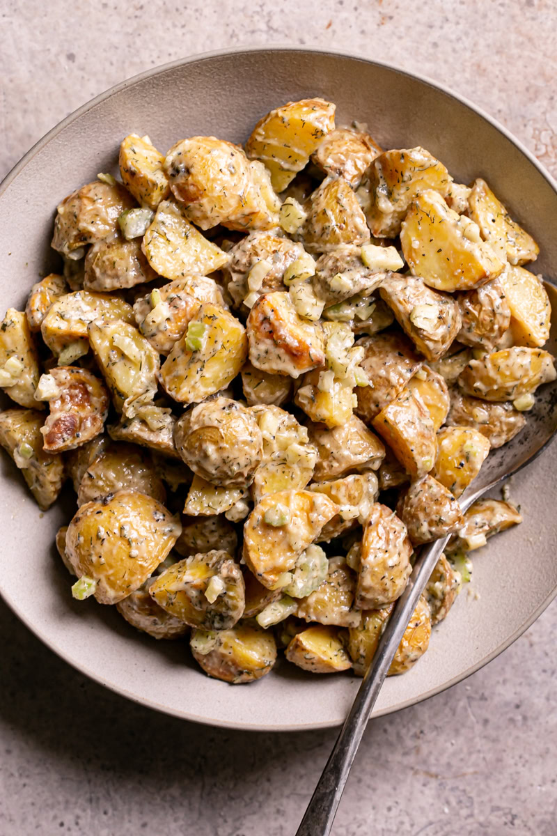 close up of a bowl of roasted caesar potato salad with a spoon in it