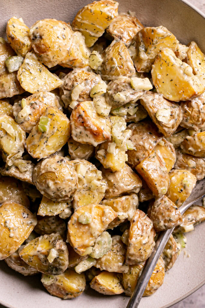 close up of a bowl of roasted caesar potato salad with a spoon in it