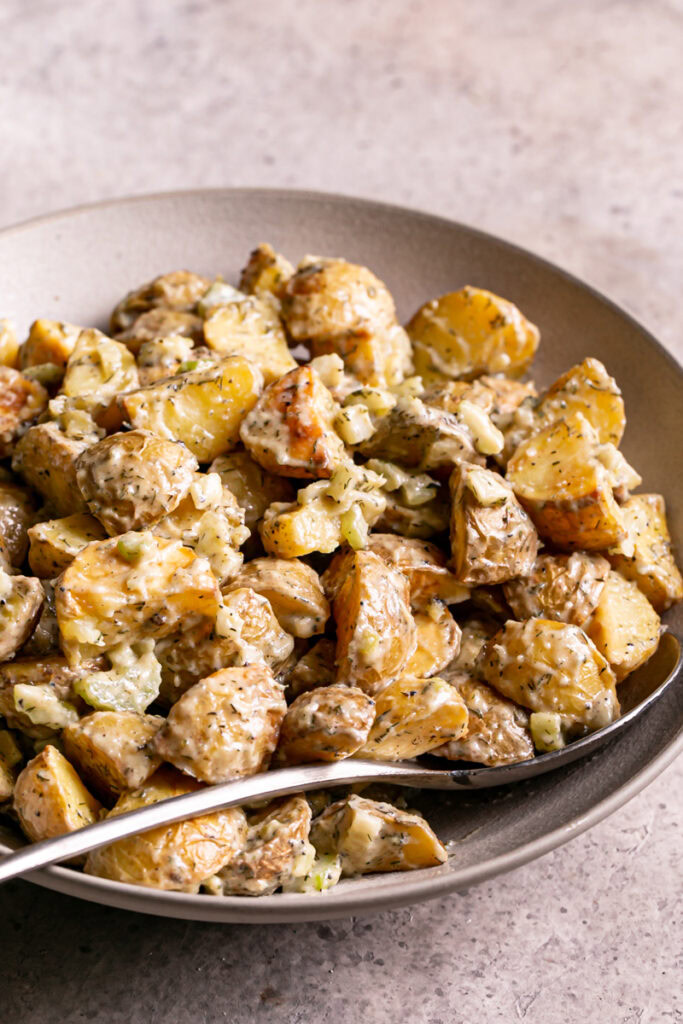 3/4 shot of close up of a bowl of roasted caesar potato salad with a spoon in it
