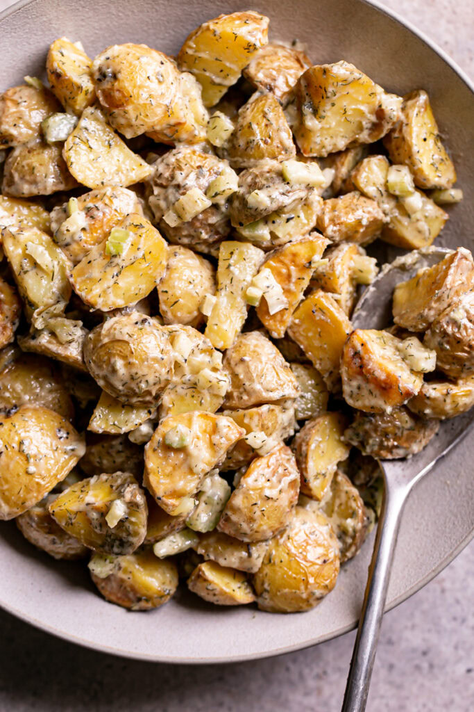 close up of a bowl of roasted caesar potato salad with a spoon in it