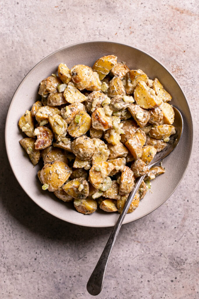 a bowl of roasted caesar potato salad with a spoon in it