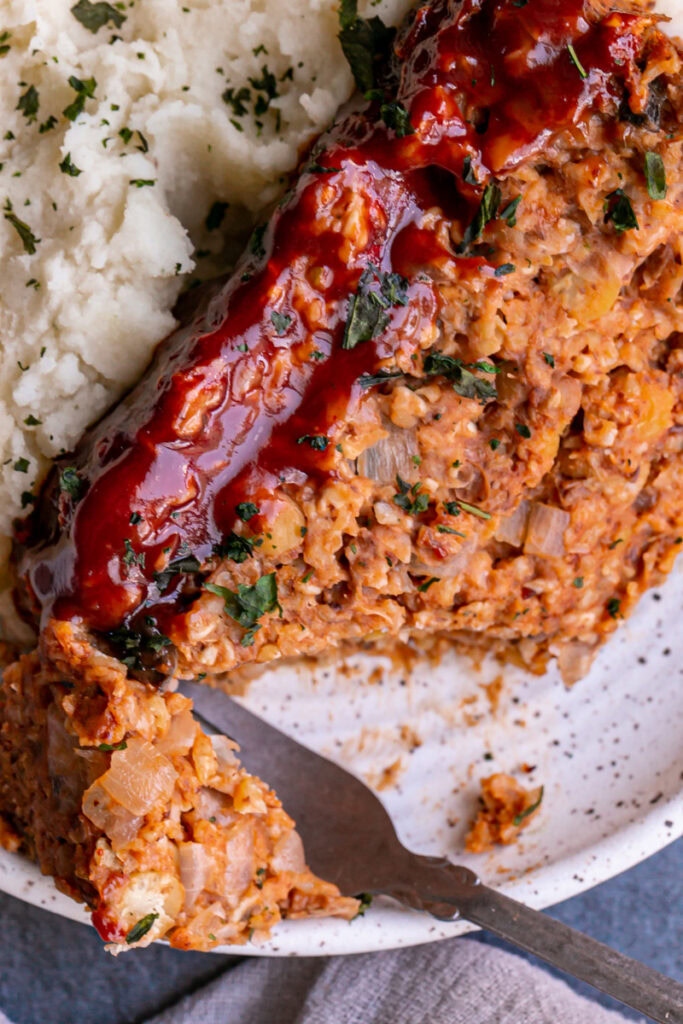close up of Vegan Gluten-Free Meatloaf on a plate with mashed potatoes and a piece of meatloaf cut off with a fork