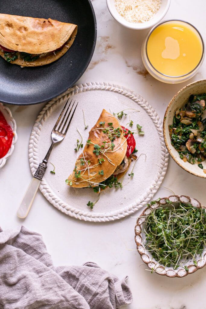 Vegan Gluten-Free Savory Pancake filled with vegan cheese, mushroom, kale and onion, and tomato on a plate garnished with fresh microgreens