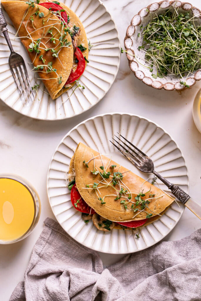two Vegan Gluten-Free Savory Pancake filled with vegan cheese, mushroom, kale and onion, and tomato on a plate garnished with fresh microgreens
