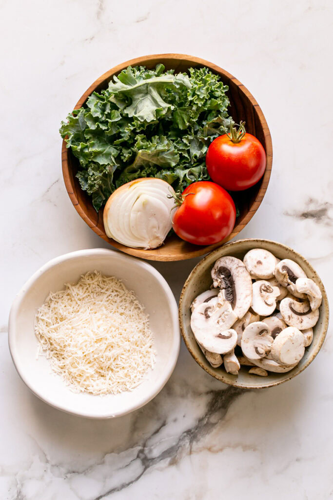 vegan gluten-free savory pancake filling produce in bowls, kale, onion tomato in one bowl, mushrooms in another bowl, and vegan cheese shreds in another bowl