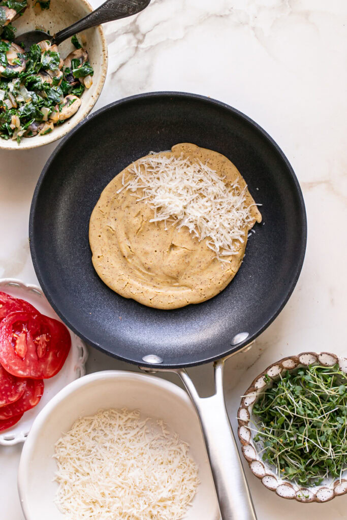 vegan gluten-free savory pancake in a skillet with vegan cheese on half of the pancake