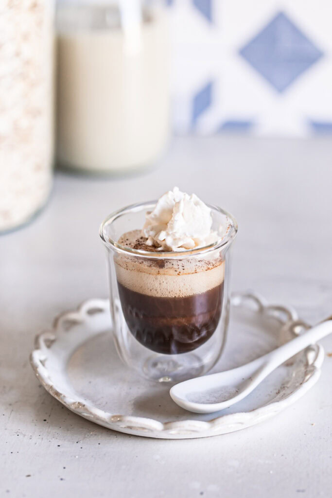 a single shot of apple crisp oat milk macchiato topped with steamed oat milk and a dollop of dairy-free whipped cream