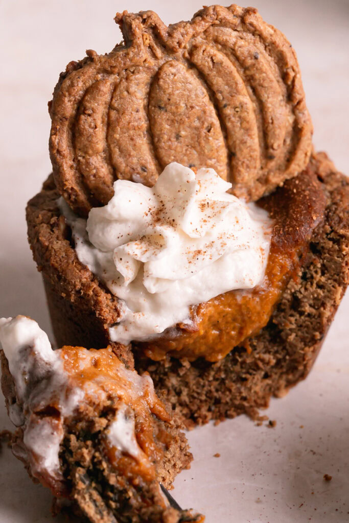pumpkin pie cookie cup topped with dairy-free whipped cream and an acorn cookie, cut open with a fork to see the pumpkin pie filling