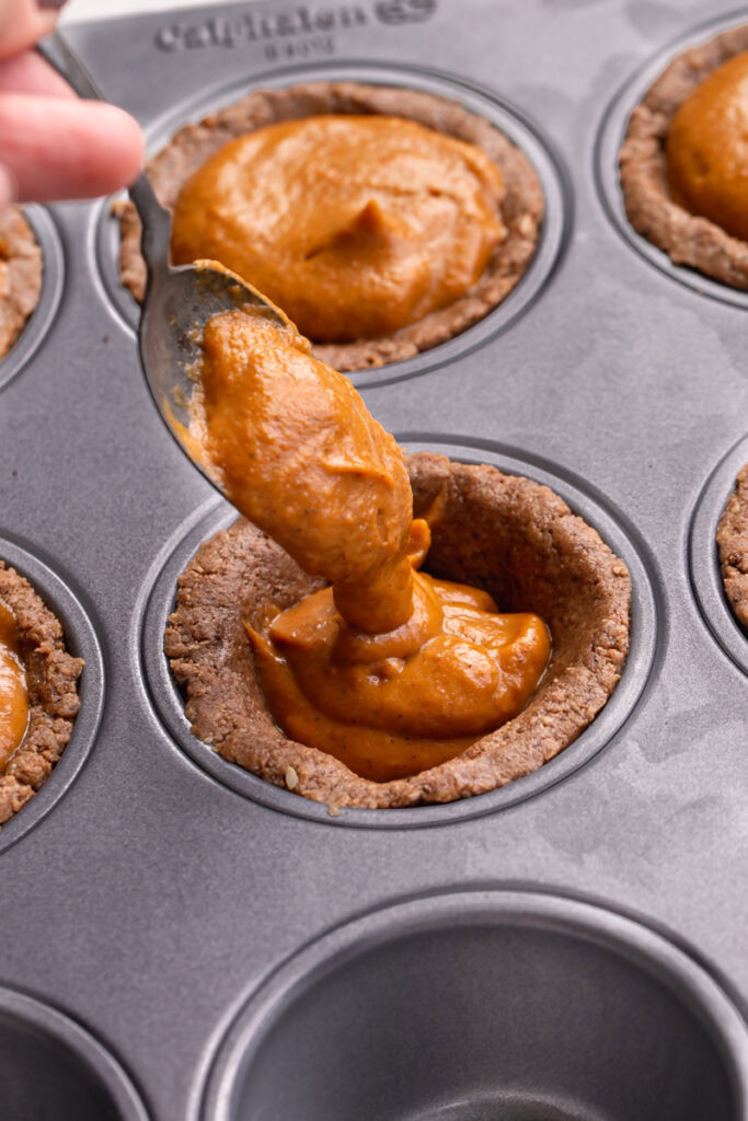 action shot of spooning the pumpkin pie filling into the cookie cups