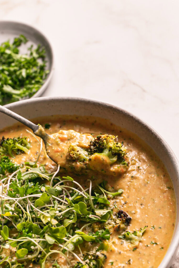 action shot of spooning some cheesy roasted broccoli potato soup out of the bowl with a spoon