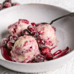 3/4 shot of three scoops of homemade dairy free cranberry swirl ice cream in a bowl with a spoon topped with sugared cranberries