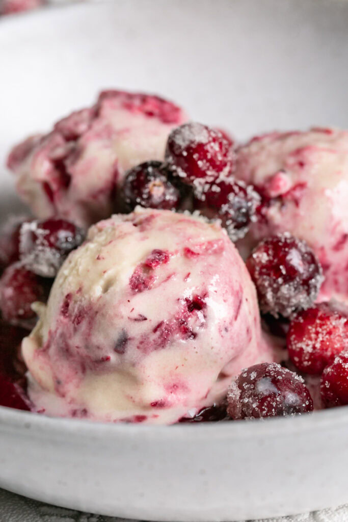 close up 3/4 shot of three scoops of homemade dairy free cranberry swirl ice cream in a bowl with a spoon topped with sugared cranberries