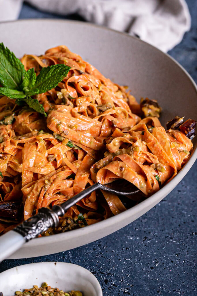 close up of raw carrot salad in a bowl garnished with fresh mint, some carrot salad twirled around a fork like pasta