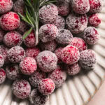 close up of sugared cranberries on a plate with a sprig of rosemary