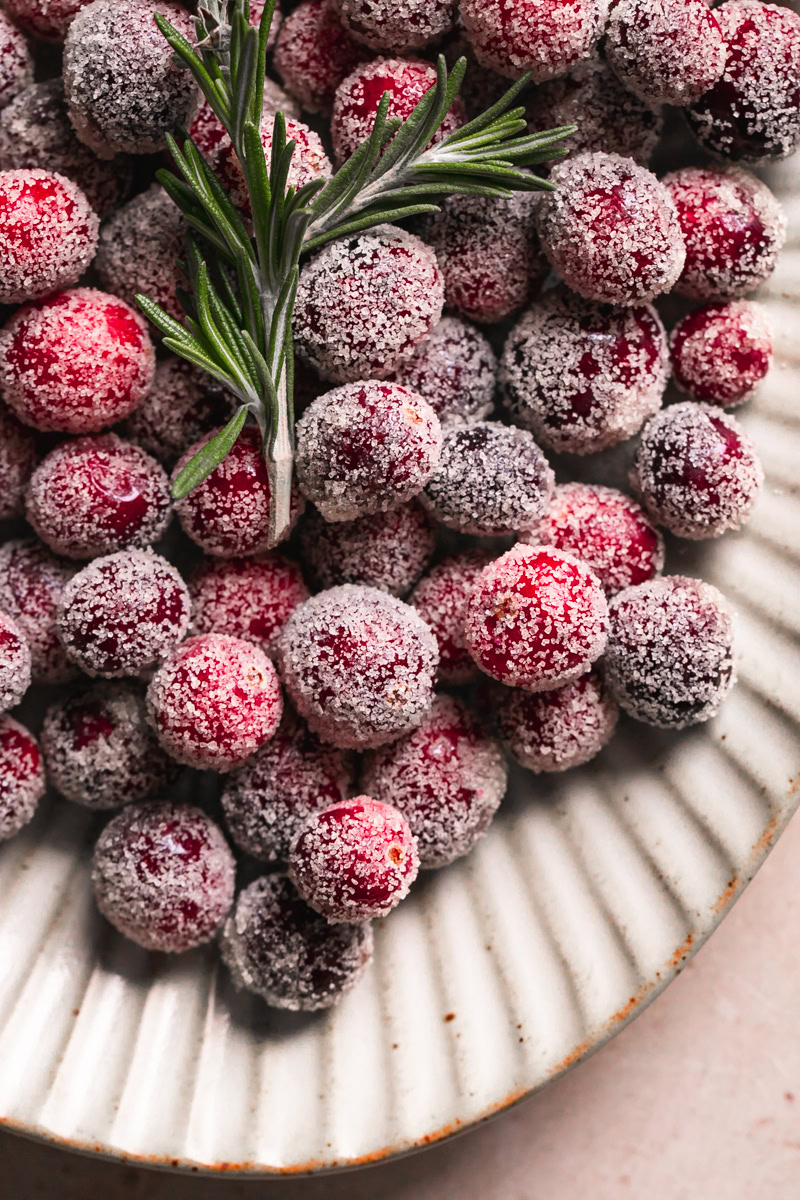 close up of sugared cranberries on a plate with a sprig of rosemary