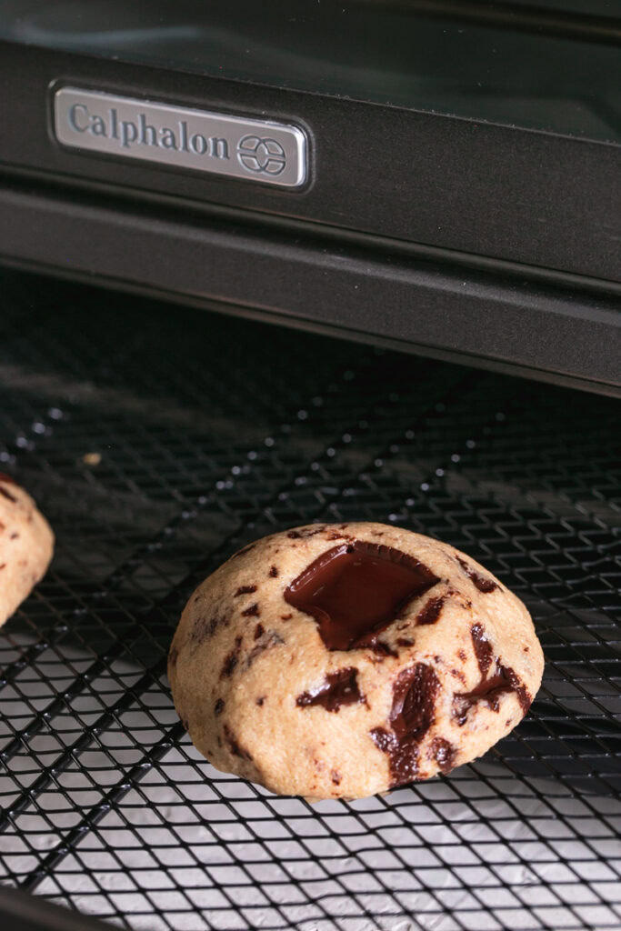 two chocolate chunk cookies on a calphalon air fryer rack sticking out of the oven