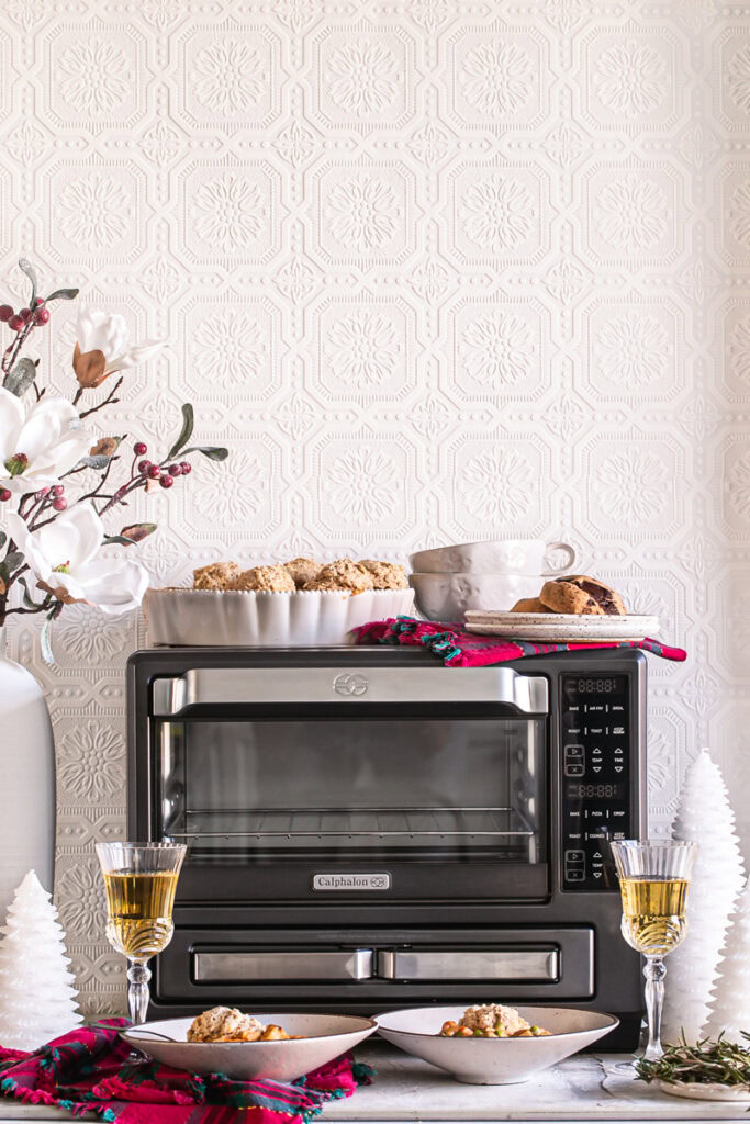 a prepared vegan dinner served in bowls sitting in front of Calphlaon Air fry oven with two glasses of wine next to it, holiday decor, and two chocolate chunk cookies on top of the oven with two mugs stacked inside one another