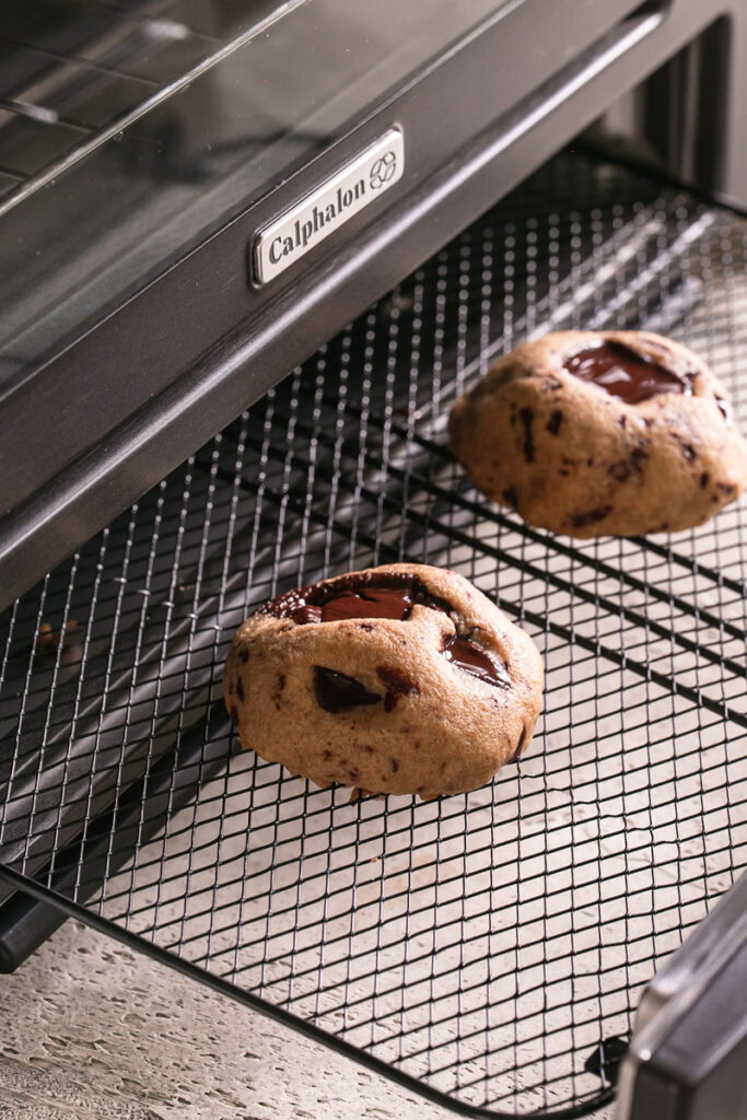 two chocolate chunk cookies on a calphalon air fryer rack sticking out of the oven