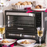 a prepared vegan dinner served in bowls sitting in front of Calphlaon Air fry oven with two glasses of wine next to it, holiday decor, and two chocolate chunk cookies on top of the oven with two mugs stacked inside one another