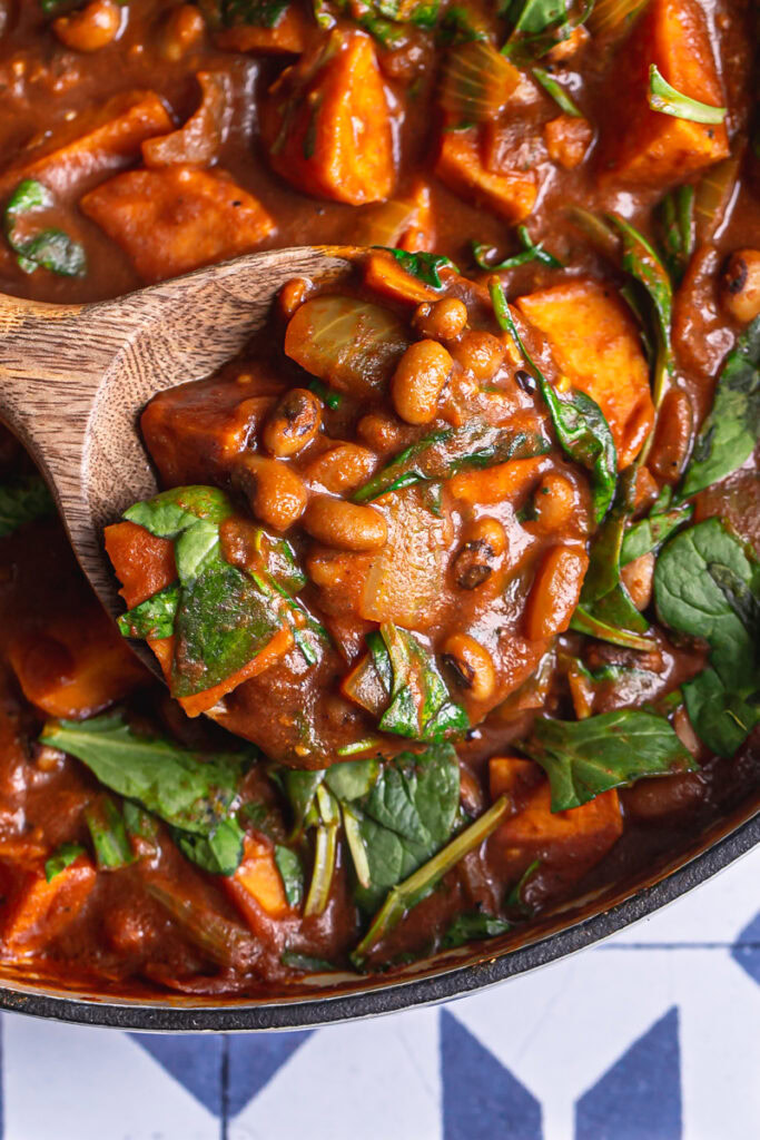 close up of a wooden serving spoon scooping up some sweet potato black eyed pea curry