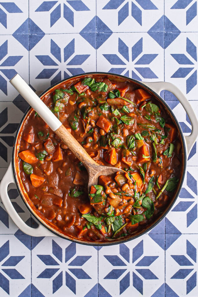 sweet potato black eyed pea curry in a white dutch oven with a wooden serving spoon in the pot