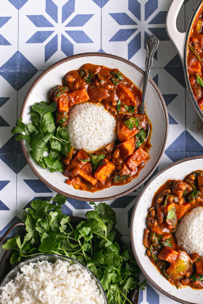 two bowls of sweet potato black eyed pea curry with spinach, a ball of white rice in the middle with fresh cilantro 
