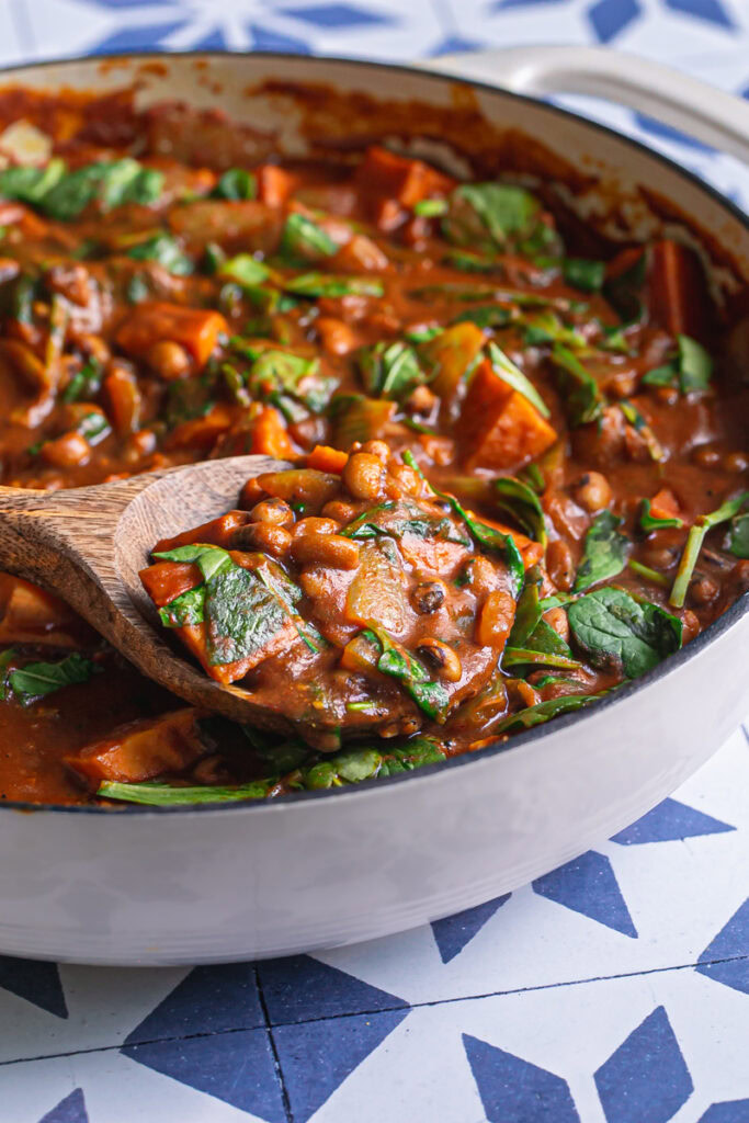 close up of a wooden serving spoon scooping up some sweet potato black eyed pea curry
